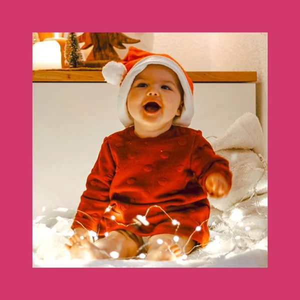 Encanto de bebê de Natal usando gorro de Papai Noel e decoração festiva.