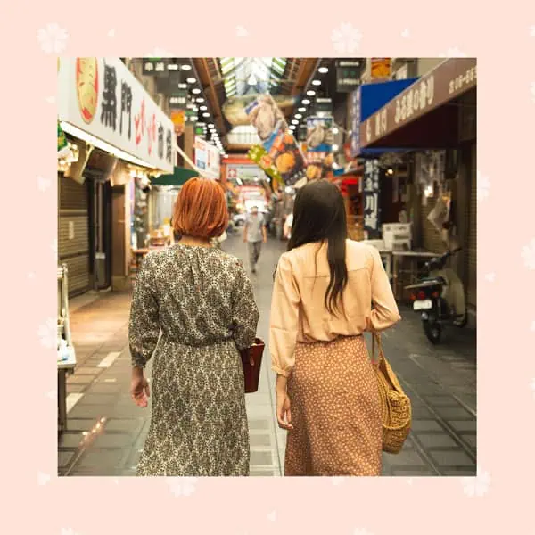 Caminhada em bairro comercial com lojas e lanternas japonesas, pessoas aproveitando passeio em atmosfera vibrante e cultural.