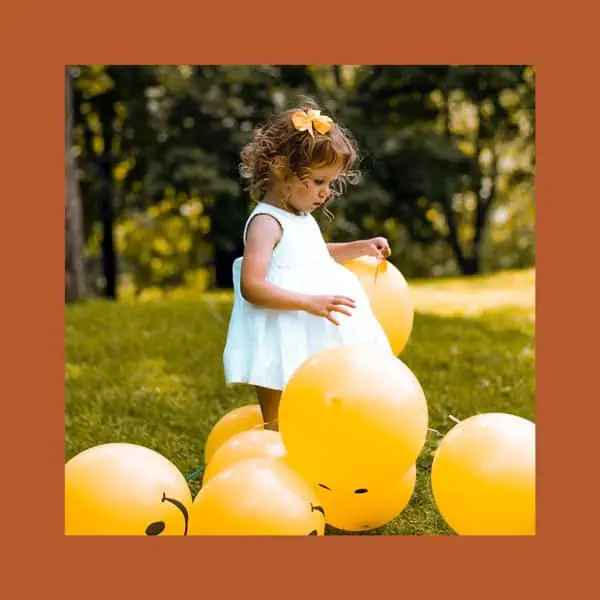 Balões amarelos de festa com criança brincando ao ar livre em parque paradisíaco.