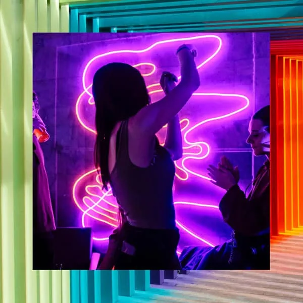 Luminária neon colorida em ambiente moderno com pessoas interagindo.