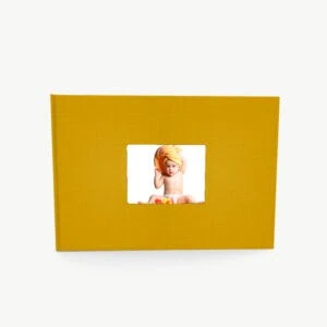 Capa de foto amarela com janela em destaque exibindo criança com touca no cabelo e sorriso feliz.